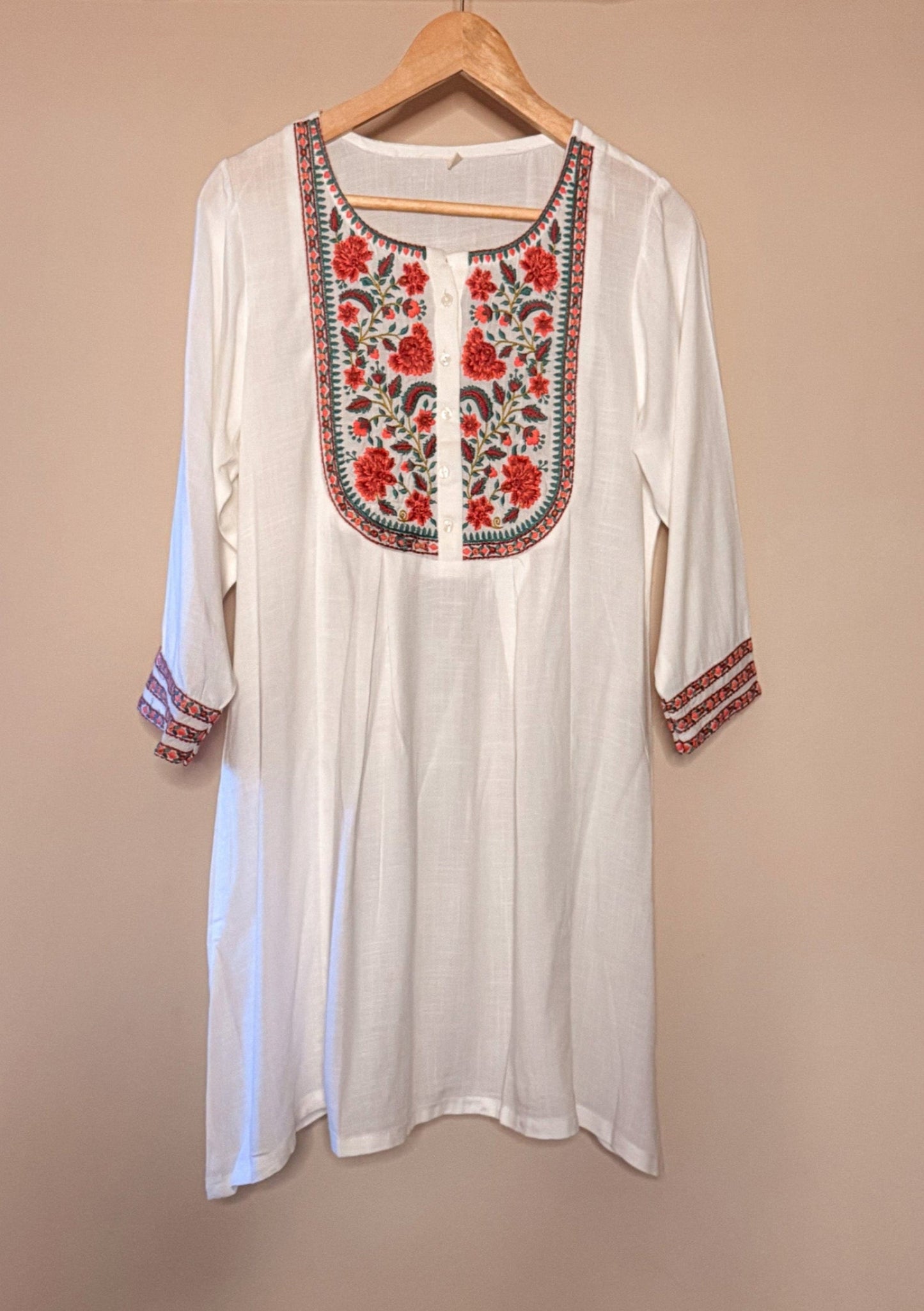 White long-sleeve top with red floral embroidery on a beige background