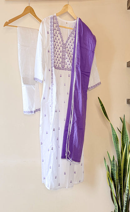 White and purple embroidered kurta with matching pants on a hanger against a beige wall.