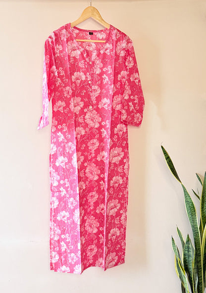 Pink floral dress hanging on a wooden hanger against a beige wall.