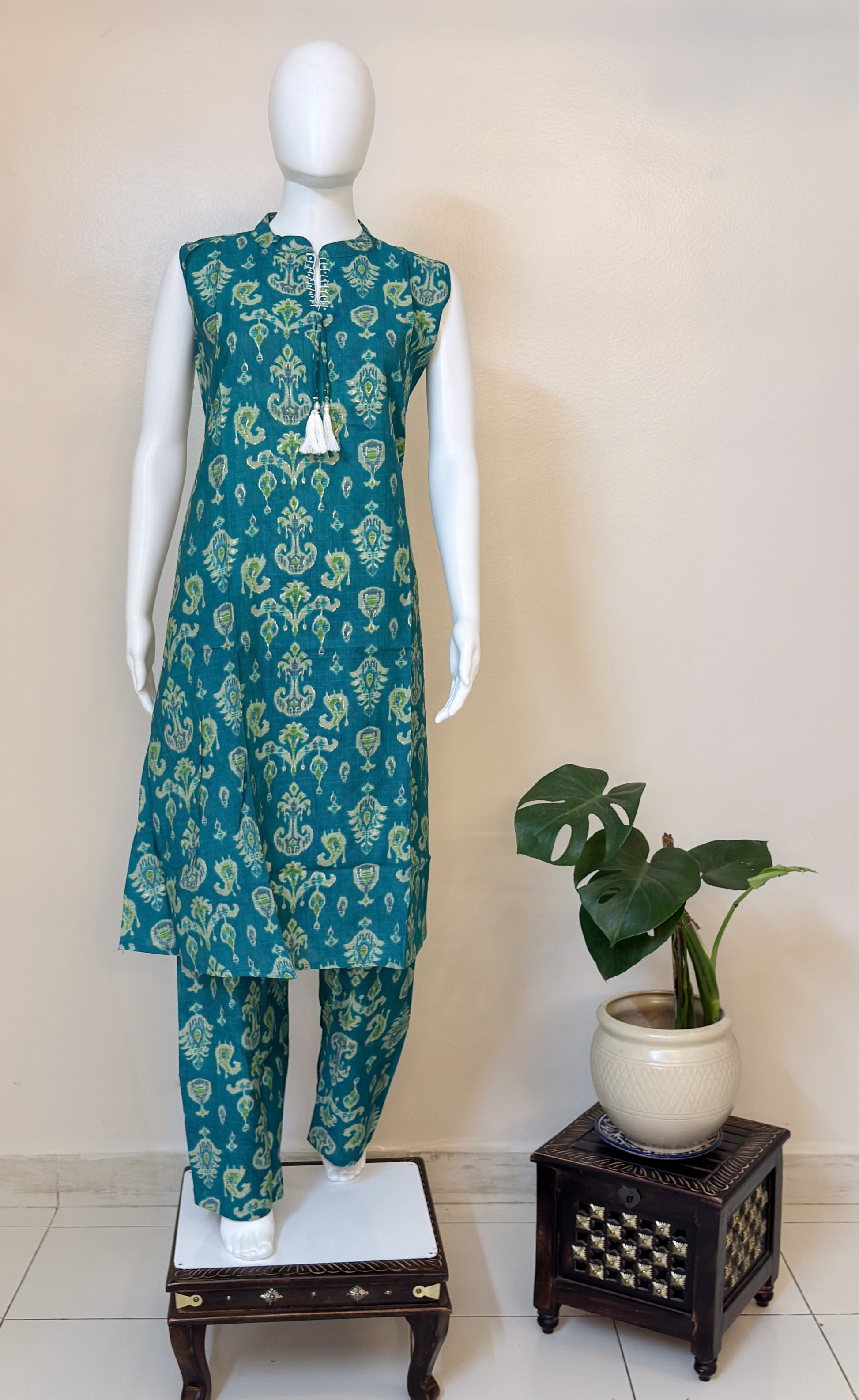 Teal green Ikat patterned kurta with pants on a mannequin next to a potted plant.